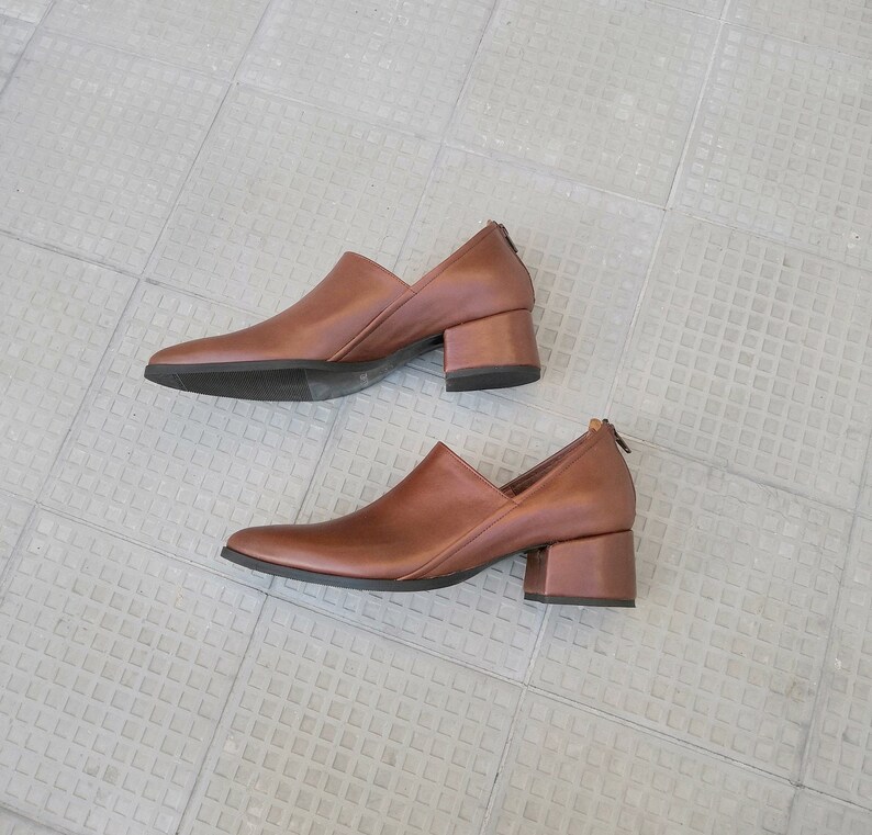May include: A pair of brown leather heeled shoes with pointed toes. The shoes have a block heel and a zipper on the back.
