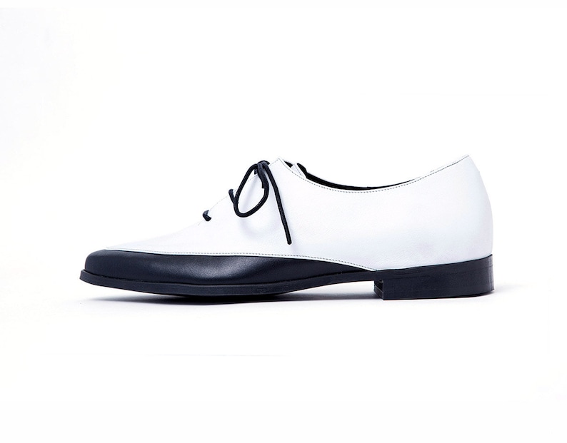 May include: White leather lace-up shoes with a black toe and heel.