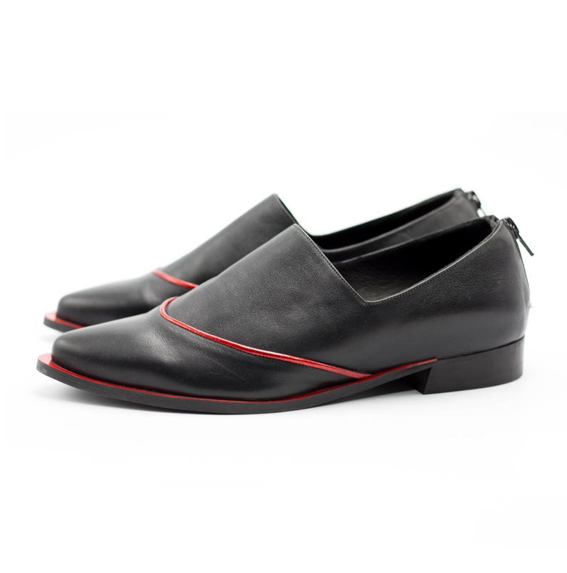 May include: Black leather slip-on shoes with a red trim around the edges. The shoes have a pointed toe and a low heel.
