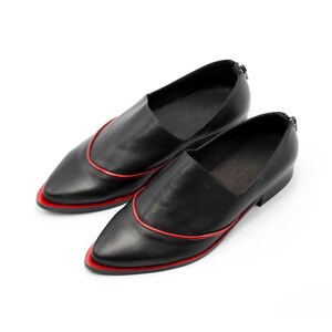 May include: Pair of black leather slip-on shoes with a pointed toe and a red trim around the edge.