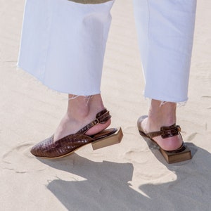 Op de afbeelding: Een paar bruine leren sandalen met hak en een gesp. De sandalen hebben een gestructureerd leren bovenwerk en een blokhak.