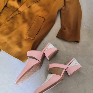 May include: A pair of pink and white heeled mules with a cutout design. The shoes have a chunky heel and a pointed toe.