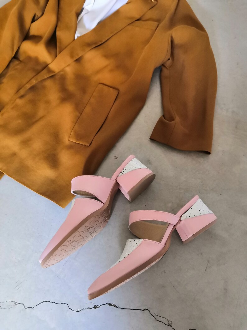 May include: A pair of pink and white heeled mules with a cutout design. The shoes have a chunky heel and a pointed toe.