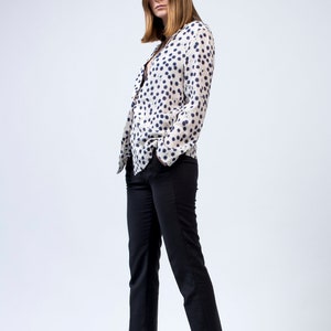 Puede incluir: Una mujer con una camisa de lunares blancos y azules, pantalones negros y zapatos negros de tac&oacute;n.
