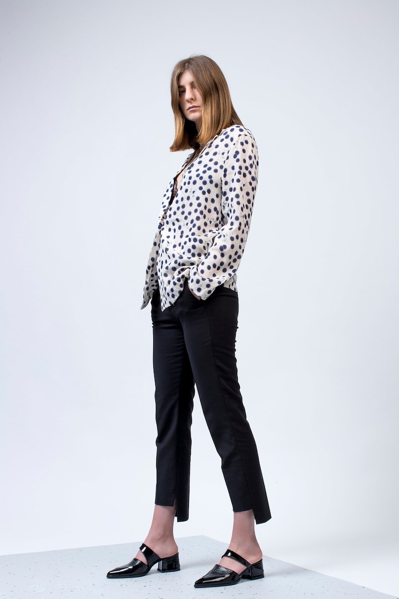 Puede incluir: Una mujer con una camisa de lunares blancos y azules, pantalones negros y zapatos negros de tac&oacute;n.