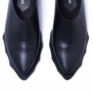 May include: A pair of black leather shoes with a pointed toe and a unique, jagged edge design on the sole.
