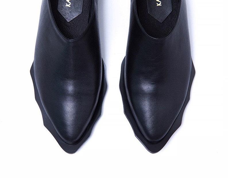 May include: A pair of black leather shoes with a pointed toe and a unique, jagged edge design on the sole.