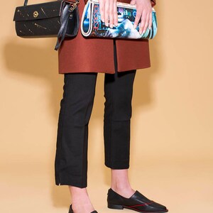 May include: A person wearing a red coat, black pants, and black shoes with red stitching. They are holding a black and gold clutch bag and a colorful clutch bag.