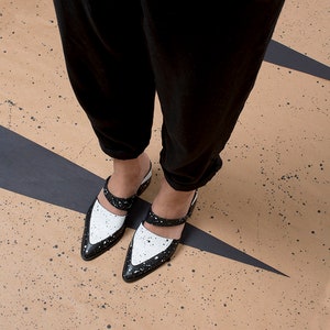 May include: A pair of black and white leather shoes with a pointed toe and a strap across the top. The shoes have a splatter paint design.