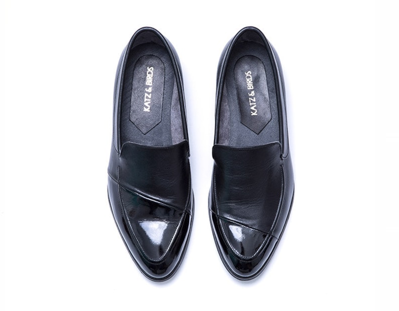 May include: A pair of black leather loafers with a patent leather toe. The loafers have a slip-on design and feature the text "KATZ & BROS" on the insole.