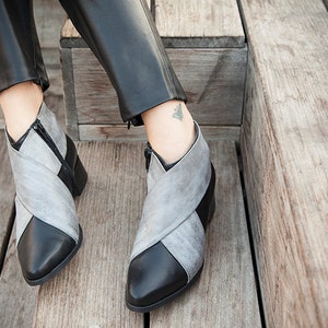 May include: A pair of gray and black ankle boots with a pointed toe and a zipper on the side. The boots are made of leather and have a criss-cross design on the front.
