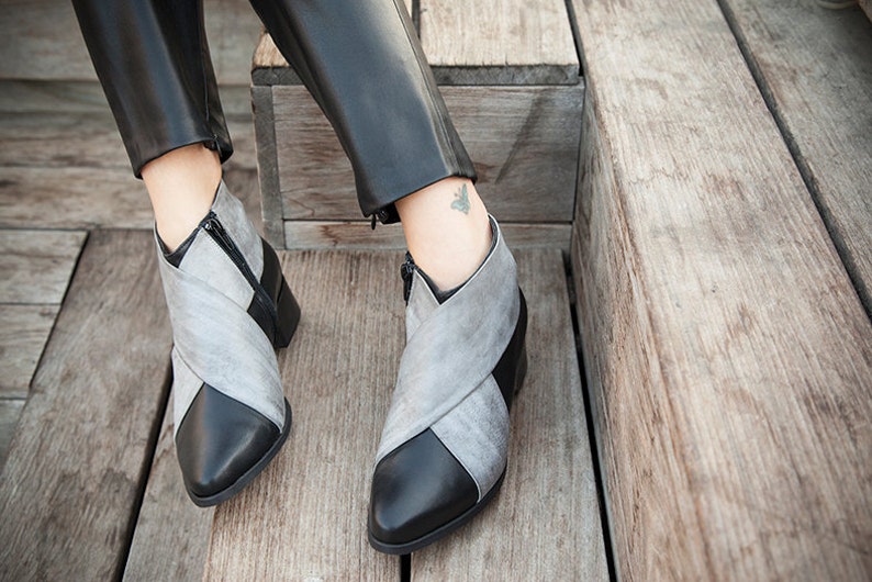 May include: A pair of gray and black ankle boots with a pointed toe and a zipper on the side. The boots are made of leather and have a criss-cross design on the front.