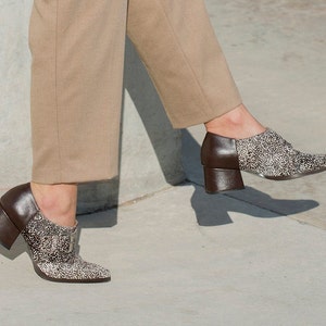 May include: A pair of brown heeled shoes with a pointed toe and a buckle detail. The shoes are covered in small white dots.