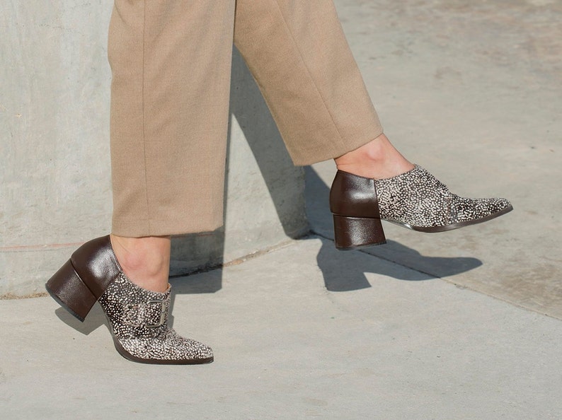May include: A pair of brown heeled shoes with a pointed toe and a buckle detail. The shoes are covered in small white dots.