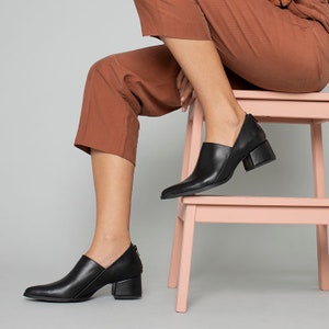 May include: Black leather ankle boots with a pointed toe and a block heel. The boots have a zipper on the inside of the ankle.