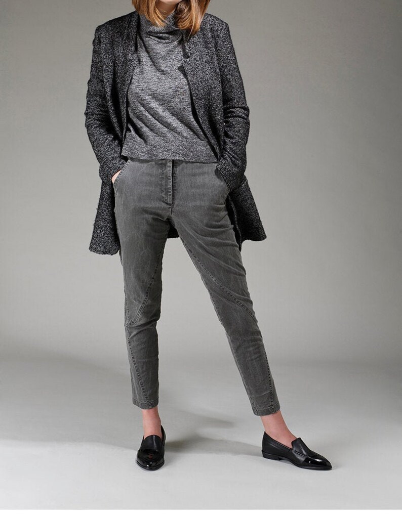 May include: A woman is wearing a gray turtleneck sweater, gray pants, and a black blazer. She is wearing black loafers.