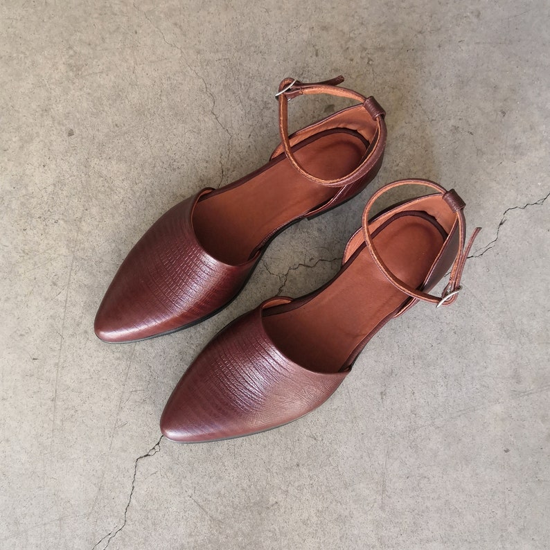 May include: A pair of brown leather ankle strap sandals with pointed toes. The sandals have a simple design and are made of a textured leather.