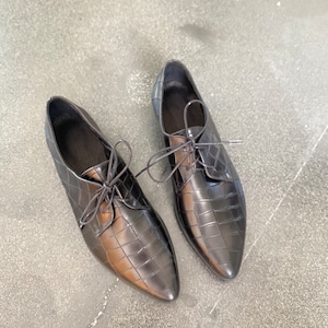 May include: A pair of black leather oxfords with a crocodile-embossed pattern and lace-up closures.