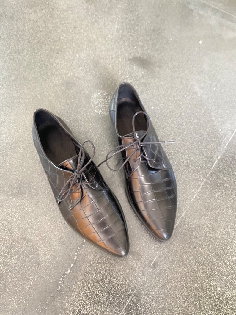 May include: A pair of black leather oxfords with a crocodile-embossed pattern and lace-up closures.