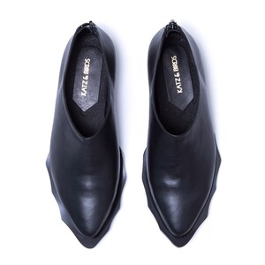 May include: A pair of black leather shoes with a pointed toe and a unique, jagged sole. The shoes have a slip-on design and feature the text "KATZ & BIRDS" on the inside.