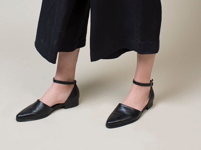 May include: Black leather ankle strap shoes with a pointed toe and a small block heel.