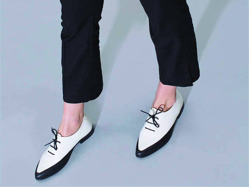 May include: White leather shoes with black trim and laces. The shoes have a pointed toe and a low heel.