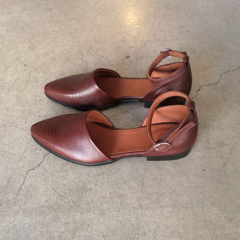 May include: A pair of brown leather ankle strap sandals with a pointed toe. The sandals have a simple design and are made of a soft, supple leather.