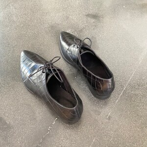 May include: A pair of black leather shoes with a crocodile-embossed pattern and lace-up closures.
