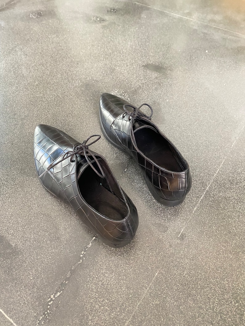 May include: A pair of black leather shoes with a crocodile-embossed pattern and lace-up closures.