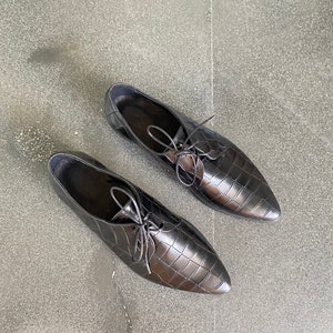 May include: A pair of black leather oxfords with a crocodile-embossed pattern and lace-up closures.
