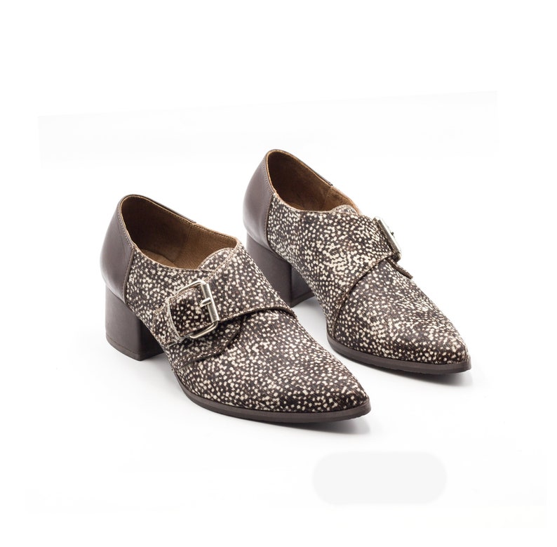 May include: A pair of brown and white patterned heeled shoes with a buckle closure. The shoes have a pointed toe and a block heel.