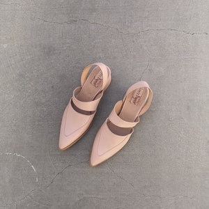 May include: A pair of light pink leather sandals with a pointed toe and ankle strap. The sandals have a simple design and are made of a soft, supple leather.