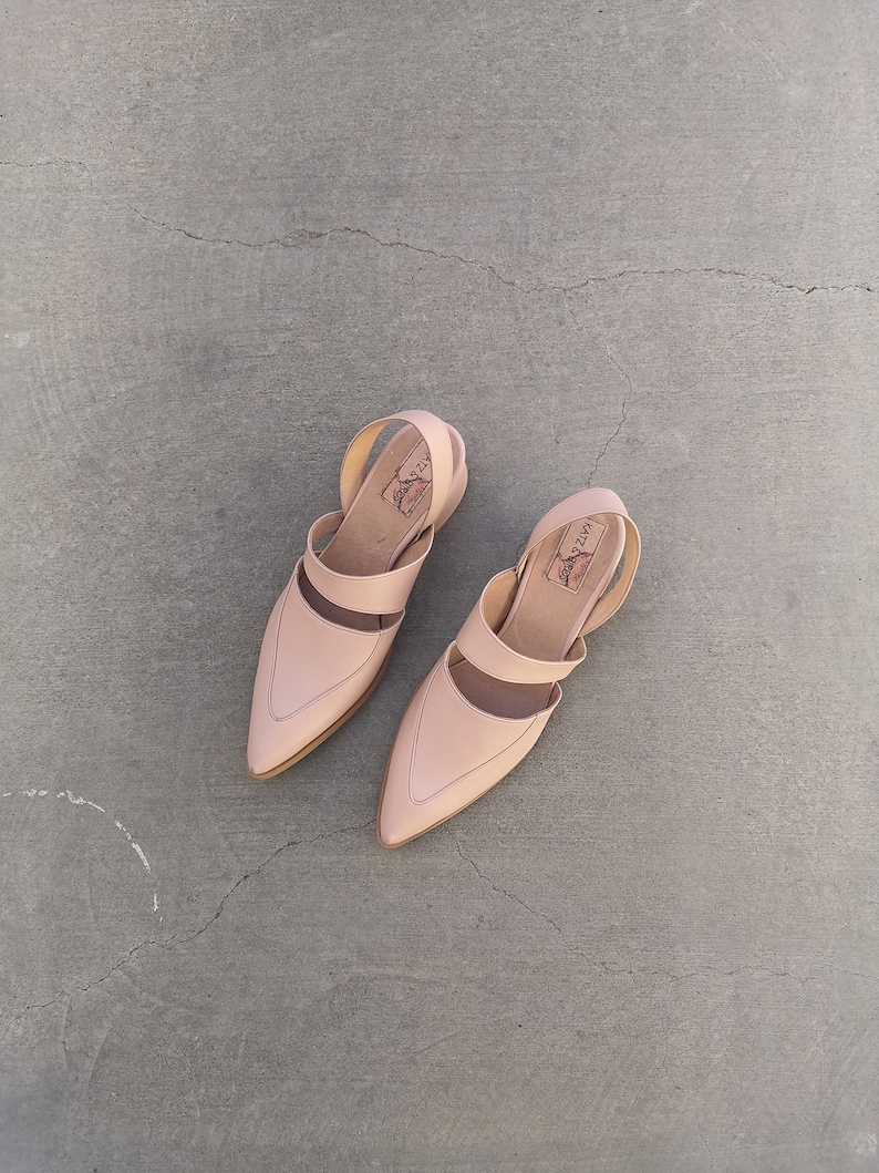 May include: A pair of light pink leather sandals with a pointed toe and ankle strap. The sandals have a simple design and are made of a soft, supple leather.