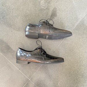 May include: A pair of black leather lace-up shoes with a crocodile-embossed pattern. The shoes have a pointed toe and a low heel.