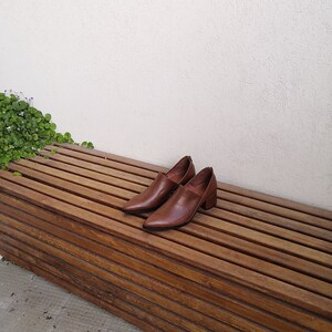May include: A pair of brown leather heeled shoes with pointed toes are sitting on a wooden bench.