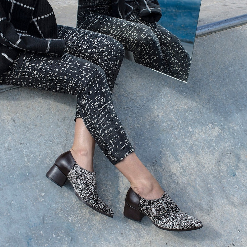 May include: A pair of black and white patterned pants with a black jacket. The person is wearing black and white shoes with a brown heel.