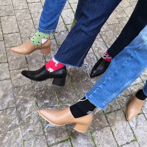May include: Three pairs of feet wearing different colored socks and heeled shoes. The shoes are brown, black, and tan. The socks are green, red, and black.
