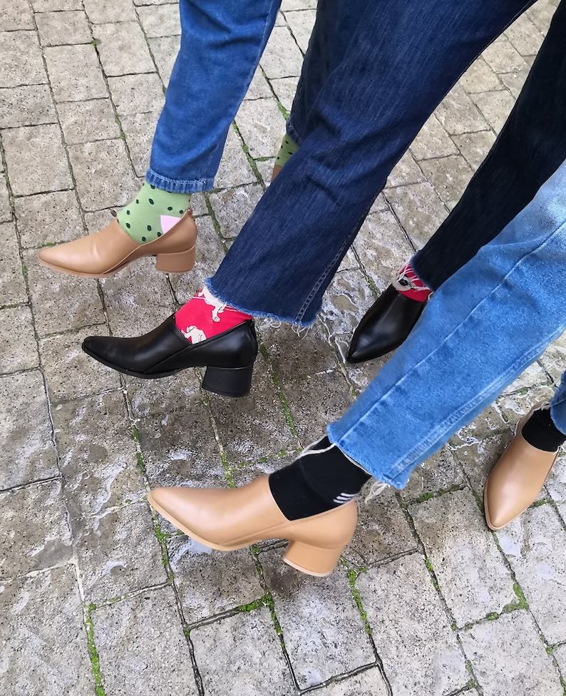May include: Three pairs of feet wearing different colored socks and heeled shoes. The shoes are brown, black, and tan. The socks are green, red, and black.