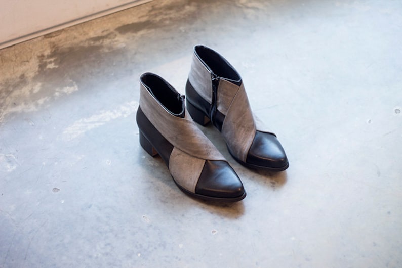 May include: A pair of gray and black ankle boots with pointed toes. The boots have a zipper on the side and a contrasting color design.
