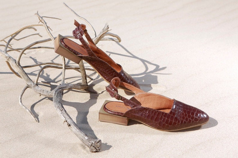 Op de afbeelding: Een paar bruine leren sandalen met hak en een krokodilpatroon. De sandalen hebben een slingback-band en een vierkante hak.