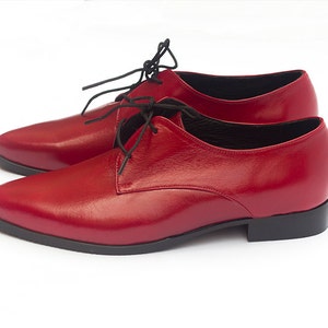 May include: A pair of red leather lace-up shoes with black laces. The shoes have a pointed toe and a low heel.