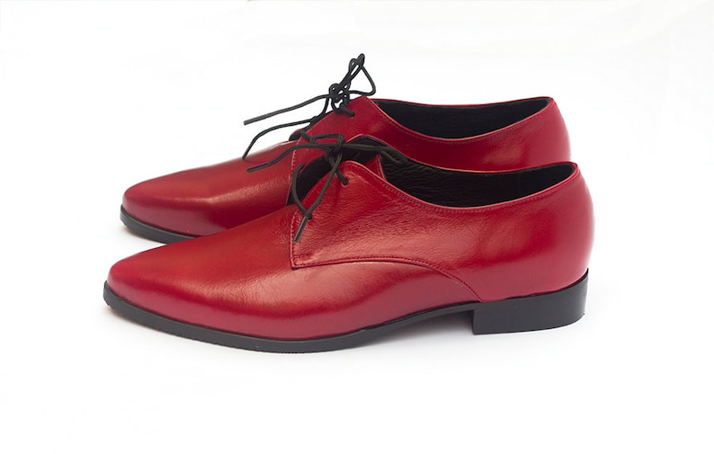 May include: A pair of red leather lace-up shoes with black laces. The shoes have a pointed toe and a low heel.