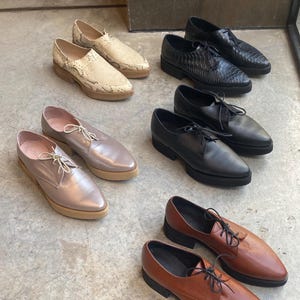 May include: Six pairs of women's leather shoes in various colours and styles. The shoes are all pointed toe and have a flat sole. The shoes are arranged in two rows of three.