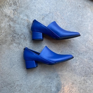 May include: A pair of blue leather heeled shoes with a pointed toe. The shoes have a block heel and a zipper on the back.
