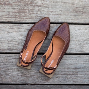 Op de afbeelding: Een paar bruine leren slingback schoenen met een krokodillenpatroon. De schoenen hebben een vierkante neus en een lage hak. De merknaam "Katz & Birds" staat op de band van elke schoen.