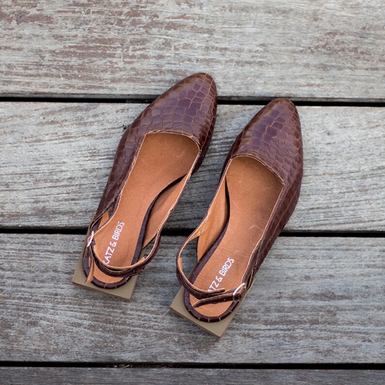 Op de afbeelding: Een paar bruine leren slingback schoenen met een krokodillenpatroon. De schoenen hebben een vierkante neus en een lage hak. De merknaam "Katz & Birds" staat op de band van elke schoen.