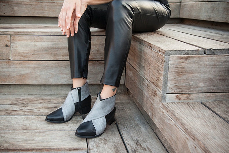 May include: A pair of gray and black ankle boots with a pointed toe and a low heel. The boots are made of leather and have a zipper on the side.