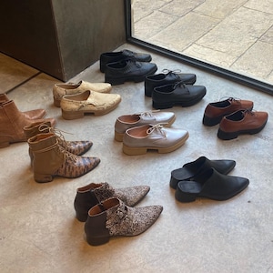 May include: A collection of various shoes and boots in different colours and styles, including brown leather boots, black leather shoes, and grey suede shoes.