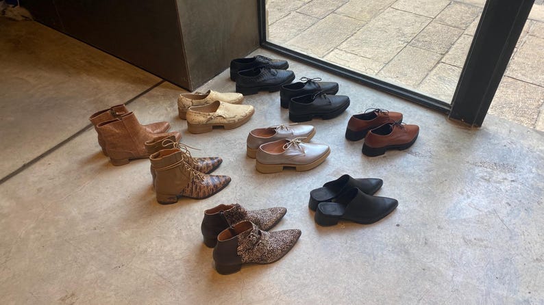 May include: A collection of various shoes and boots in different colours and styles, including brown leather boots, black leather shoes, and grey suede shoes.