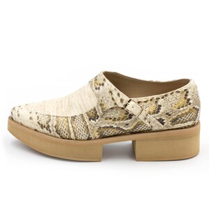 Puede incluir: Un par de zapatos de plataforma beige con estampado de piel de serpiente y una hebilla.